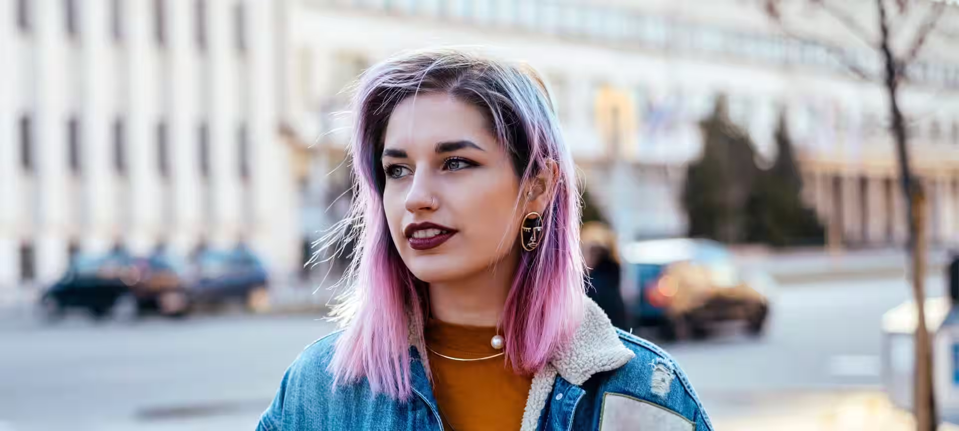 young woman in denim jacket with pink hair and dark roots